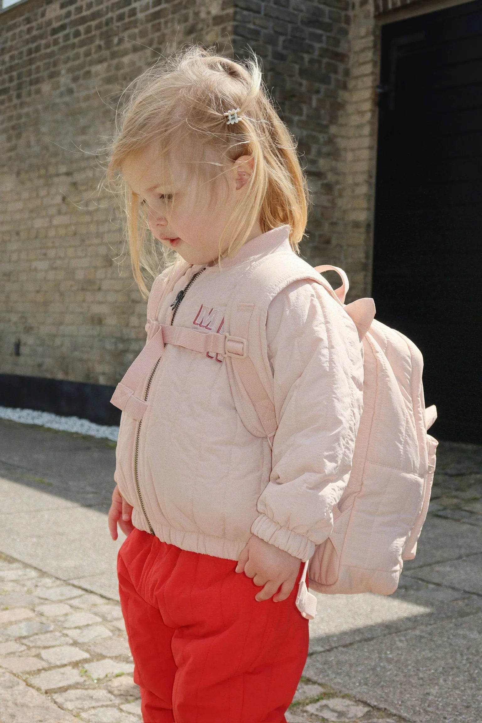 Side view of child wearing Konges Sløjd Juno Kitty backpack in peachy pink