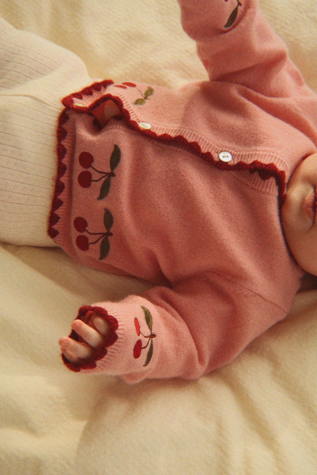 Baby lying on a bed wearing the pale blush cherry cardigan