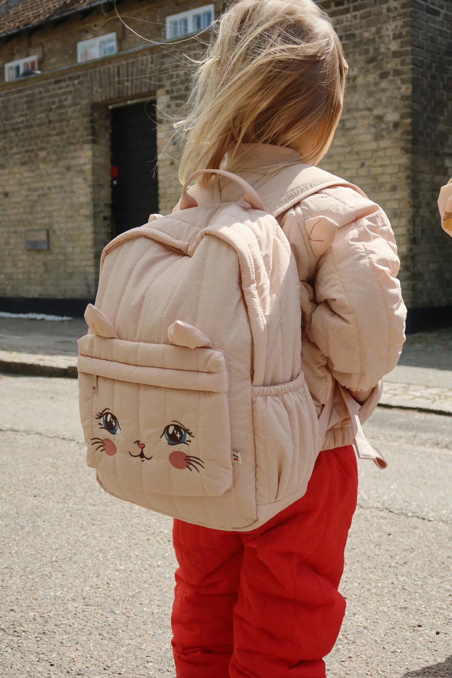 Child outdoors wearing Konges Sløjd Juno Kitty backpack in peachy pink