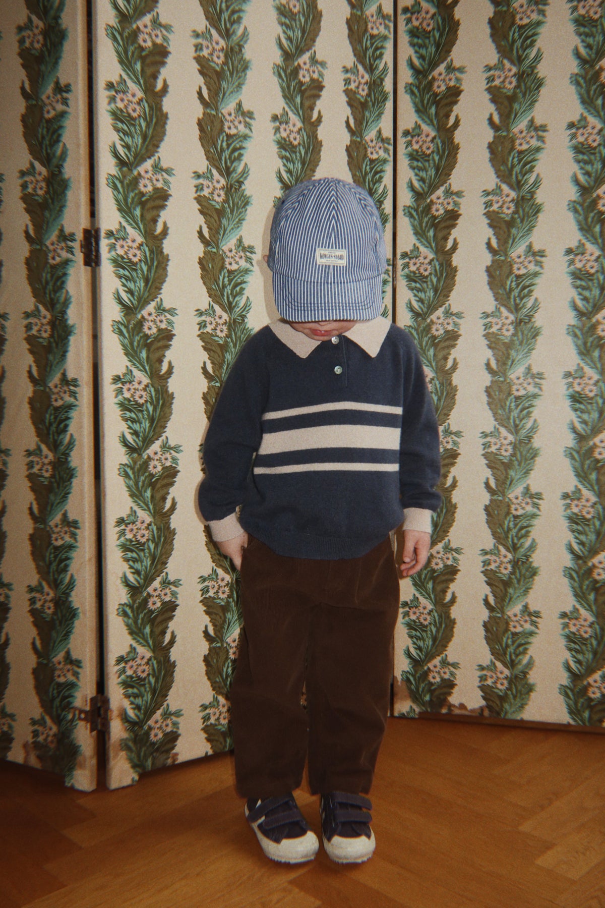 Child wearing the navy striped Basi polo with brown corduroy pants and a cap
