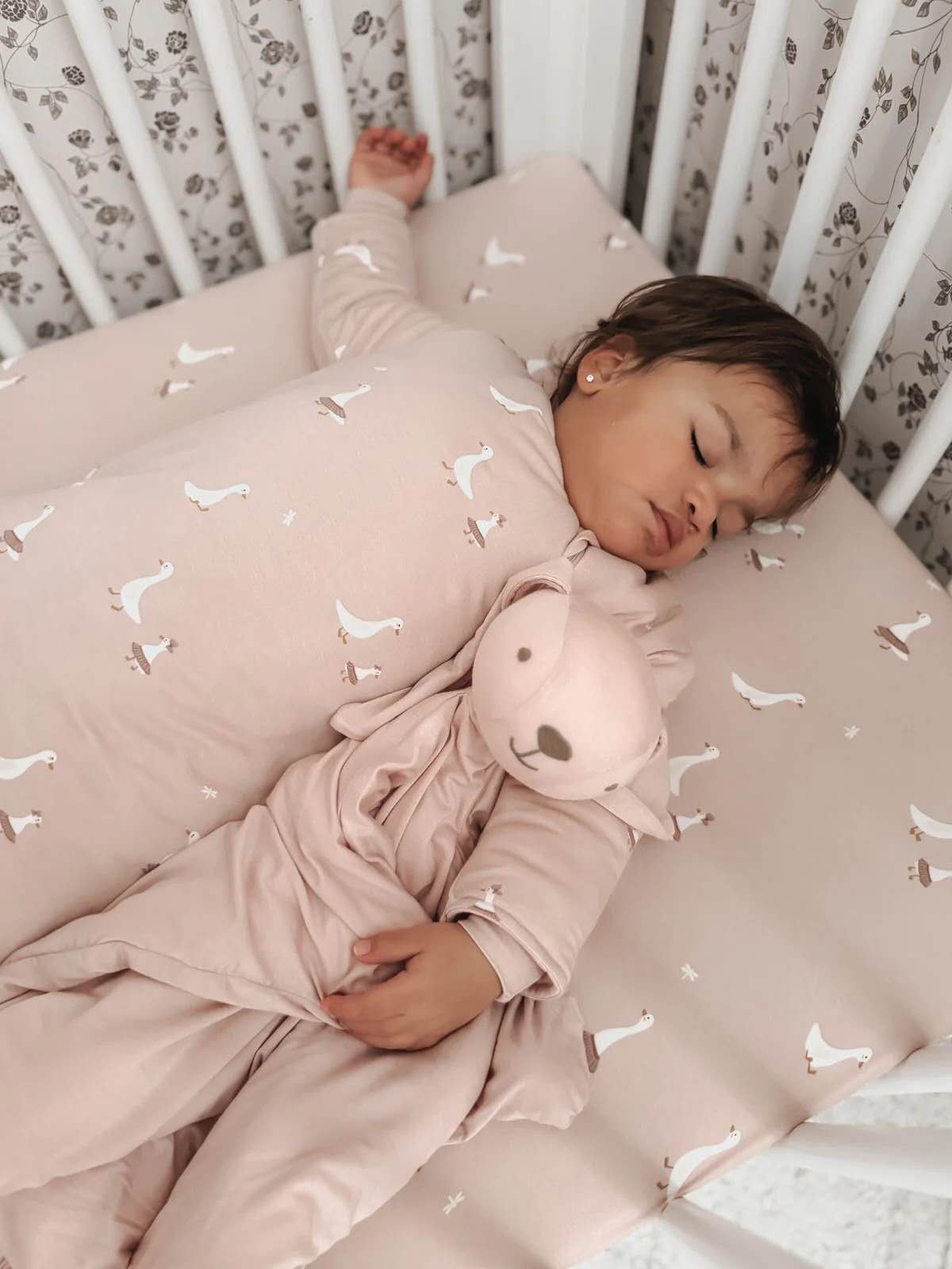 gūnamūna Bunny Lovey Stella — soft blush pink plush bunny lovey shown with sleeping newborn in cot